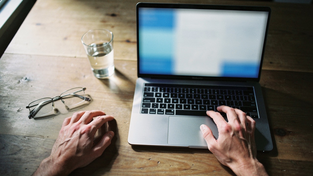 Hands on a laptop beside a glass of water