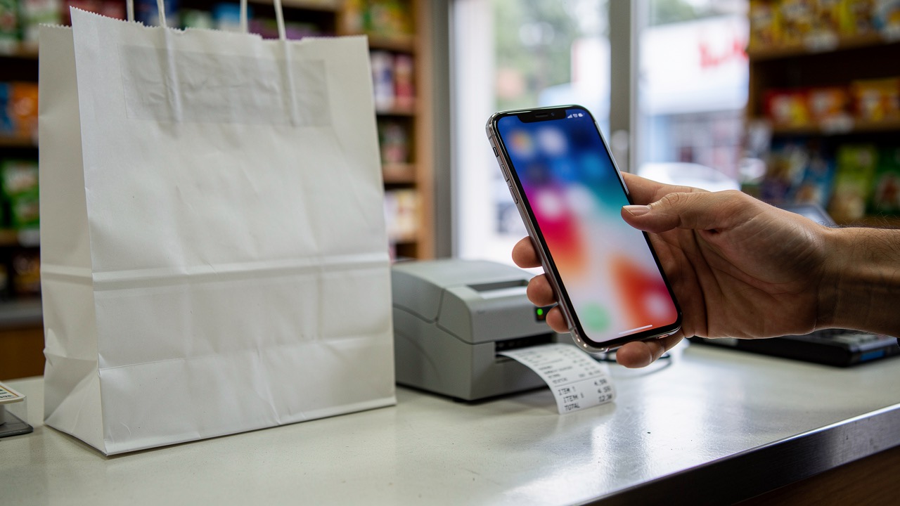 Phone held at a shop counter next to a paper bag